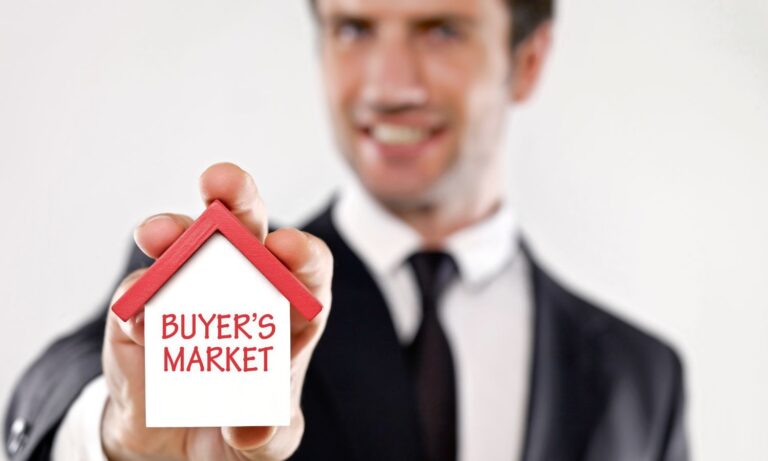 Man in a suit holding a small house model with the words 'Buyer's Market' written on it