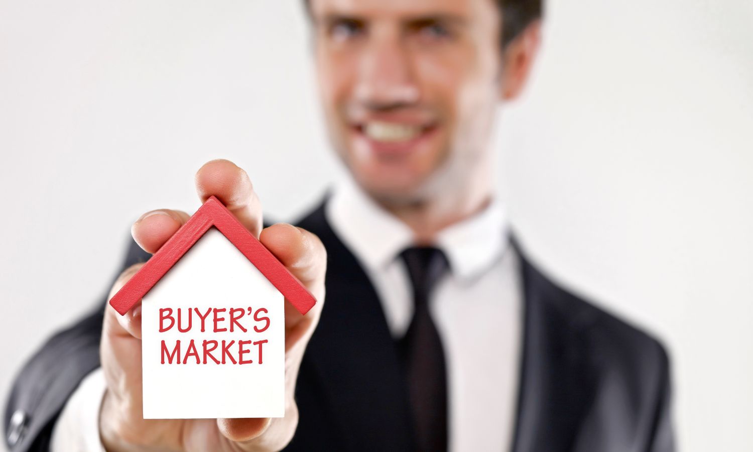 Man in a suit holding a small house model with the words 'Buyer's Market' written on it