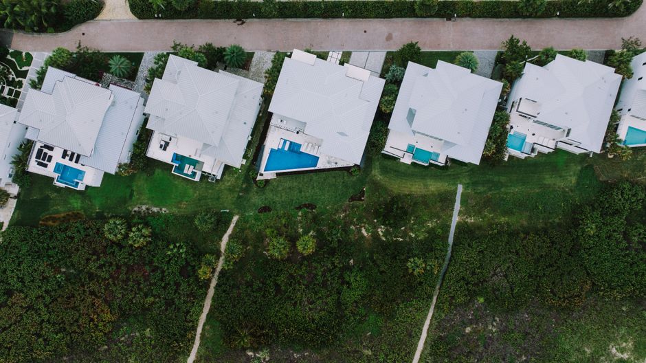 An aerial drone shot of a large, upscale home surrounded by a vast, manicured green lawn and mature trees, illustrating the concept of valuable acreage.